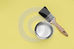 Can with white paint and brush on yellow background, flat lay. Space for text