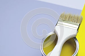 A can of yellow paint with a brush on a gray-yellow with a white background