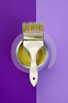 A can of yellow paint with a brush on a purple background