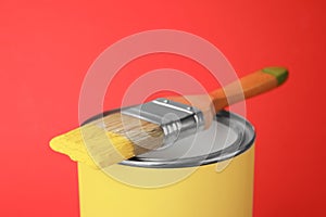 Can of yellow paint with brush on red