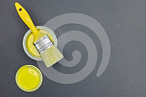 Can of yellow paint and paintbrush on gray background. top view
