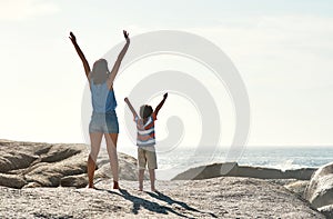 Can you feel the sun in your bones. a parent with their child raising their arms in the sunlight at the beach.
