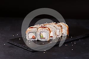 Canada eel sushi rolls with cucumber and salmon on a stone plate over black background