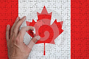 Canada flag is depicted on a puzzle, which the man`s hand completes to fold