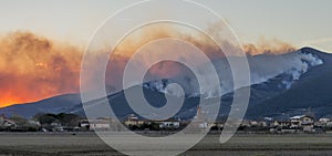 Canadair flies over a small town at sunset during a fire extinguishing operation due to natural disaster