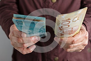 Canadian Dollars and Brazilian currency. Front view of old woman`s hand handling bills