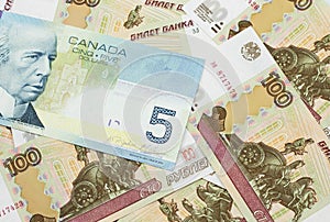 A Canadian five dollar bill on a background of dollar bills