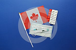 Canadian flag and face mask, antipyretic pill treatment, syringe and thermometer on blue background