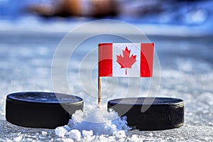 Kanadská vlajka na párátko mezi dvěma hokejovými puky. Kanada bude hrát na mistrovství světa ve skupině A. 2019 IIHF World