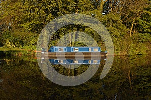 Canal barge narrow boat reflected in water surrounded by trees