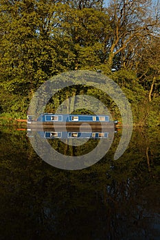 Canal barge narrow boat reflected in water surrounded by trees