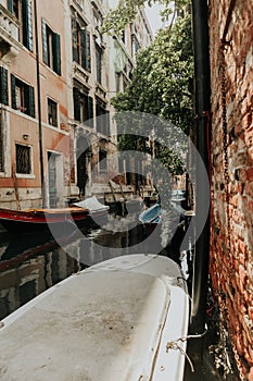 Canal between brick buildings with boats on shore, surrounded by trees, Venice, italy