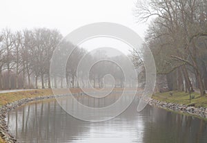 Canal lined with trees on a gray and foggy winter day