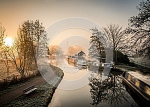 Canal narrow river boats at foggy dawn sunrise with beautiful mist orange haze wood burning smoke from chimneys silhouette trees photo
