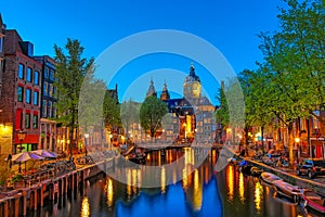 Canal and St Nicholas Church in Amsterdam at twilight, Netherlands. Famous Amsterdam landmark near Central Station.