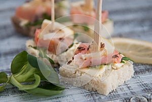 Canape with Salmon Fish Pieces, Butter Cream, White Bread and Arugula Leaves. European food. Wooden Gray Background.