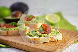 Canape sandwich with avocado cream or guacamole and tomatoes freshly prepared with ingredients on a rustic wooden kitchen