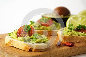 Canapes with avocado cream or guacamole and tomatoes freshly prepared with ingredients on a kitchen board, gray white