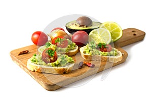 Canapes with avocado cream or guacamole and tomatoes freshly prepared with ingredients on a kitchen board, isolated on a white ba