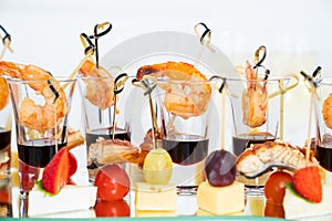 canapes of cheese with fruit, fish with tomatoes and shrimp with sauce in glass.