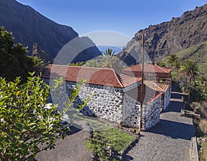 Tenerife view on old stone house in Masca village with palm tees, beatiful green sharp cliff, sea horizon and blue sky background