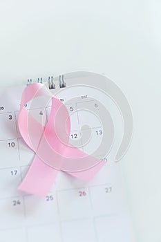 Cancer concept : Pink ribbon symbol of breast cancer and calendar on black stone board background