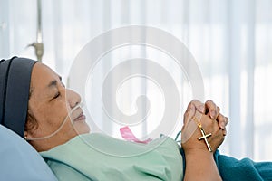 Cancer patient during chemotherapy treatment with headscraf and ink ribbon on shirt lying on hospital bed with cross on hand to