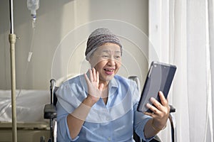 Cancer patient woman wearing head scarf making video call on social network with family and friends in hospital