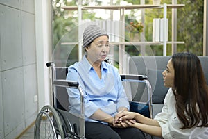 Cancer patient woman wearing head scarf sitting on wheelchair talking to her supportive daughter indoors, health and insurance