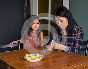 Candid asian family mom and daughter in kitchen at home, mother gives treat to girl at table, cozy apartment lifestyle