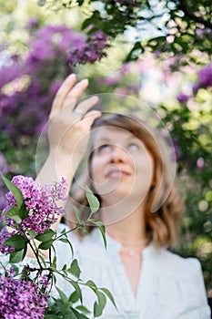 Candid authentic portrait of 30s 40s caucasian blonde woman with lilac flowers. 30 40 year old woman enjoying life in