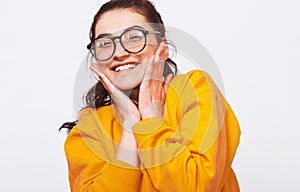 Candid close up portrait of beautiful young woman, smiling broadly, wears orange sweater and round transparent spectacles. Pretty