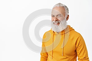 Candid happy old man with long stylish beard, laughing and smiling, looking happy, wearing modern orange hoodie