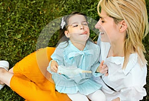 Candid image of happy mother playing with her daughter outdoors. Cute little girl eating cotton candy with her mom,