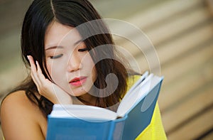 Candid lifestyle portrait of young beautiful and relaxed Asian Korean student girl on reading book or studying outdoors at coffee