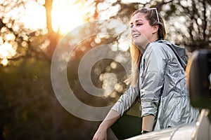 Candid lifestyle portrait of a woman outdoors in nature on road trip adventure journey, sitting on hood of car