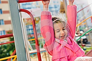 Candid outdoor image of happy little girl smiling broadly, wearing pink outfit posing outside at playground. Cheerful child