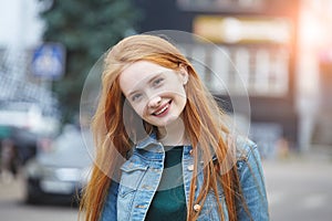 Outdoor portrait of pretty smiling young girl with long red hair, morning sunrise light