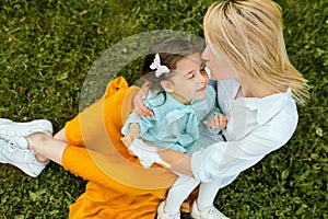 Candid outdoors image of beautiful mother playing and cuddling with her daughter, enjoying the time together.