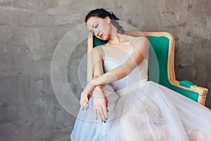 Candid portrait of Ballet dancer ballerina in beautiful light blue dress tutu skirt posing sitting on vinage chair in loft studio
