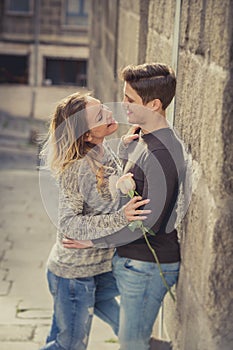 Candid portrait of beautiful European couple with rose in love kissing on street alley celebrating Valentines day