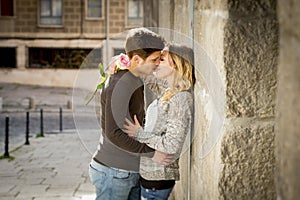 Candid portrait of beautiful European couple with rose in love kissing on street alley celebrating Valentines day