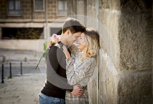 Candid portrait of beautiful European couple with rose in love kissing on street alley celebrating Valentines day