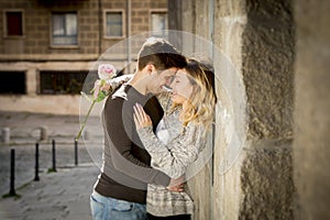 Candid portrait of beautiful European couple with rose in love kissing on street alley celebrating Valentines day