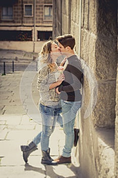 Candid portrait of beautiful European couple with rose in love kissing on street alley celebrating Valentines day
