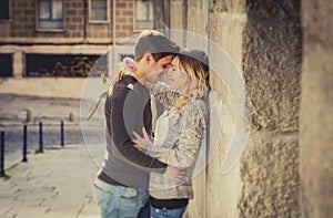 Candid portrait of beautiful European couple with rose in love kissing on street alley celebrating Valentines day photo