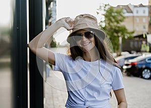 Candid portrait of beautiful young brunette woman wearing hat and sunglasses enjoying summer in city
