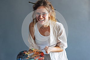 Candid portrait of a happy artist female painting on canvas in her art studio. A cheerful professional young woman painter in