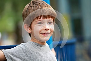 Candid portrait of a happy boy in grey t shirt smiling and sitting on the bench outdoor in the park whose front top milk teeth out