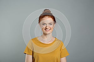 Candid portrait of happy red haired woman with charming smile on grey background